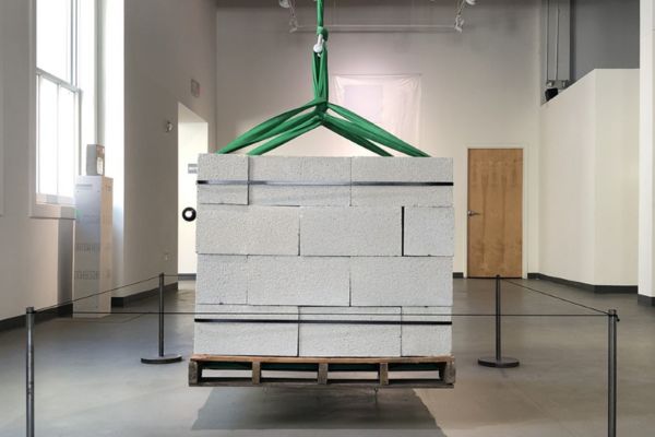 one ton of cinder blocks stacked on a wood pallet hangs from the museum ceiling