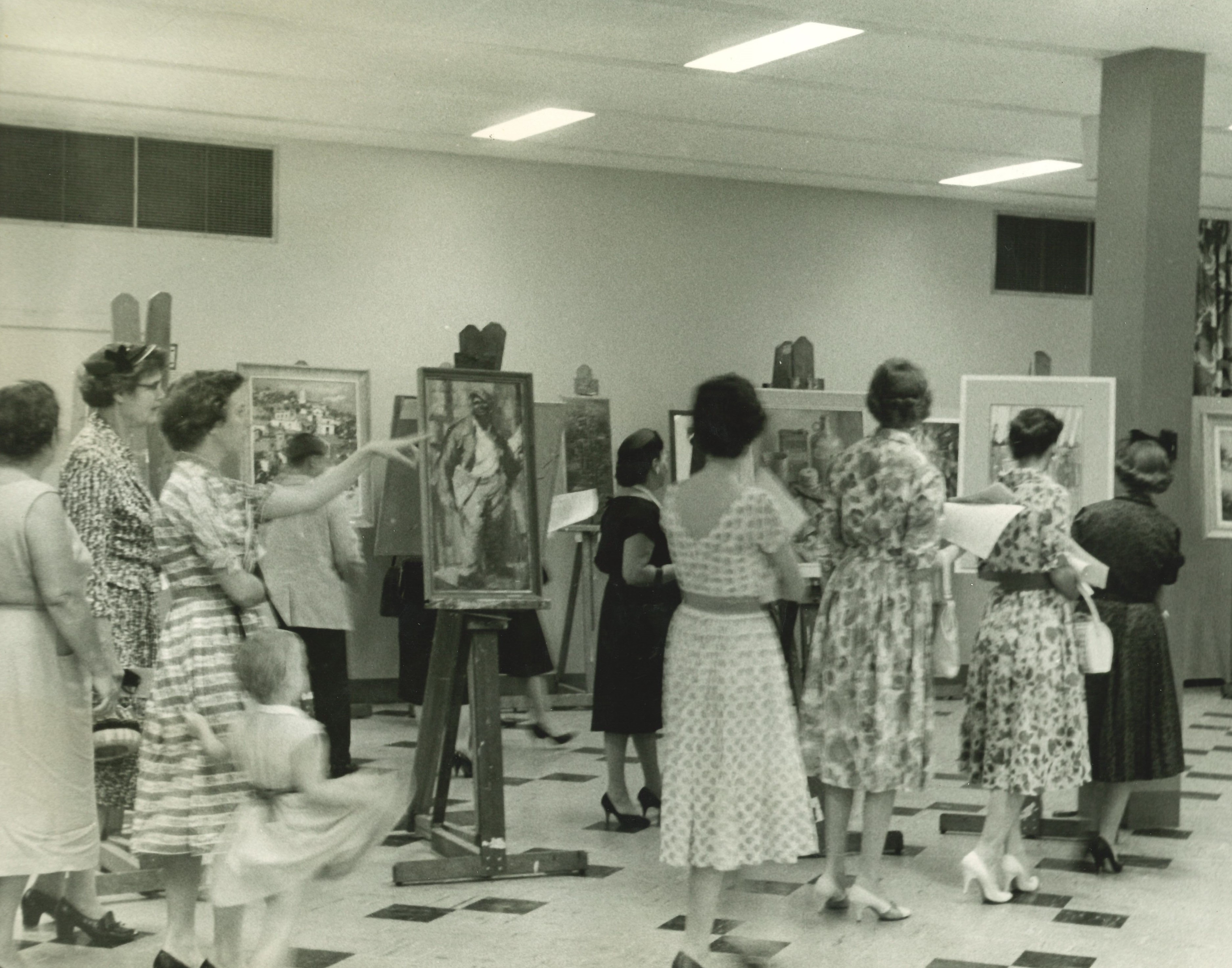 a group of women look at paintings on display in the 1950s
