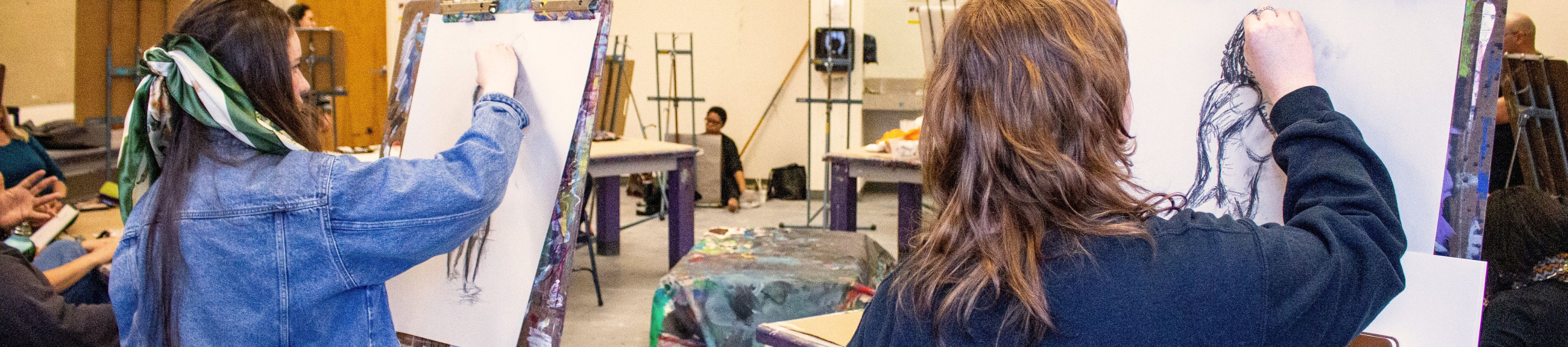 two people in a figure drawing class with large easels 