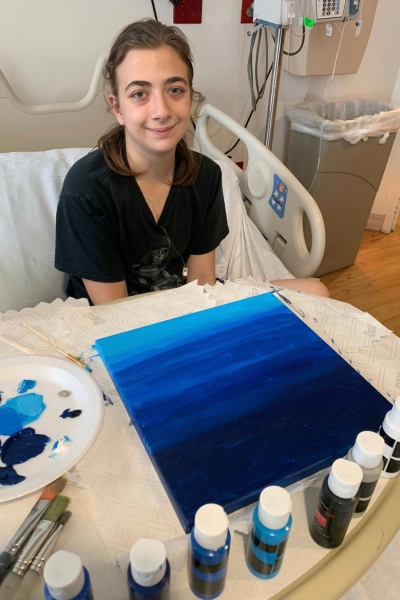 a teen smiling and posing with their artwork, which features a painted blue gradient 