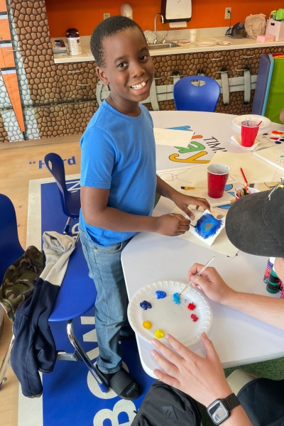child smiling and posing with their artwork, which features a blue mask