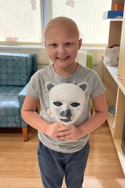 a child smiling and posing with their artwork, a mask that looks like a polar bear