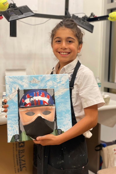 a child smiling and posing with their artwork, a mask that looks like a ninja