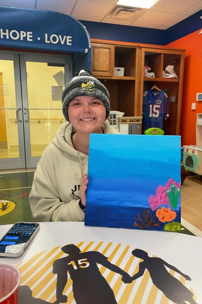 a teen smiling and posing with their artwork that is inspired by the ocean