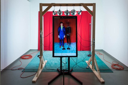 large monitor in front of a red curtain and overhead lamps