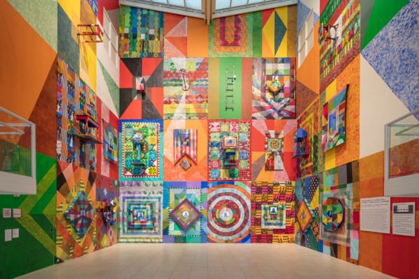 artwork by Carl Joe Williams featuring vibrantly painted walls that look like quilts dotted with tv screens