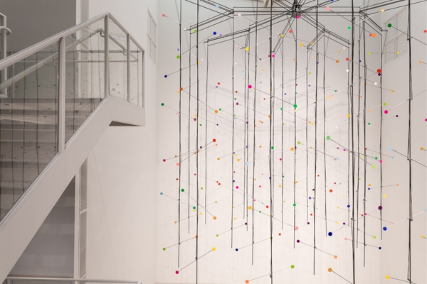 kinetic sculpture by Juan Fontanive featuring hanging rods with circles that change from white to colors