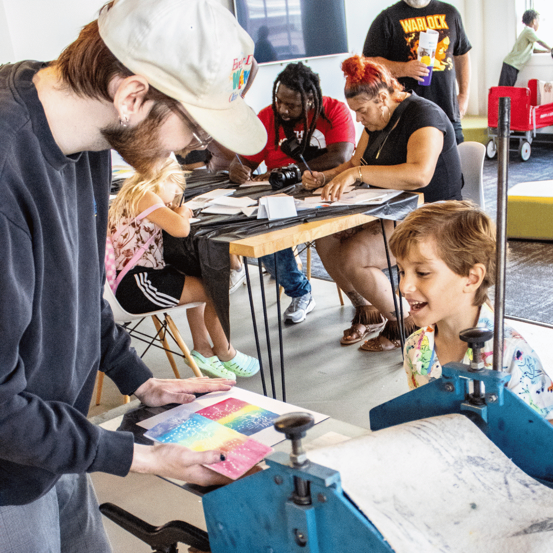a UNF printmaking students teaches a kids how to use a printing press during MOCA Family Day