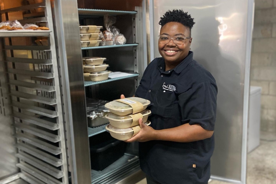 Chef Shantrell Mixon of SoulFULL Eats smiling and holding up a stack of meal-to-go packages