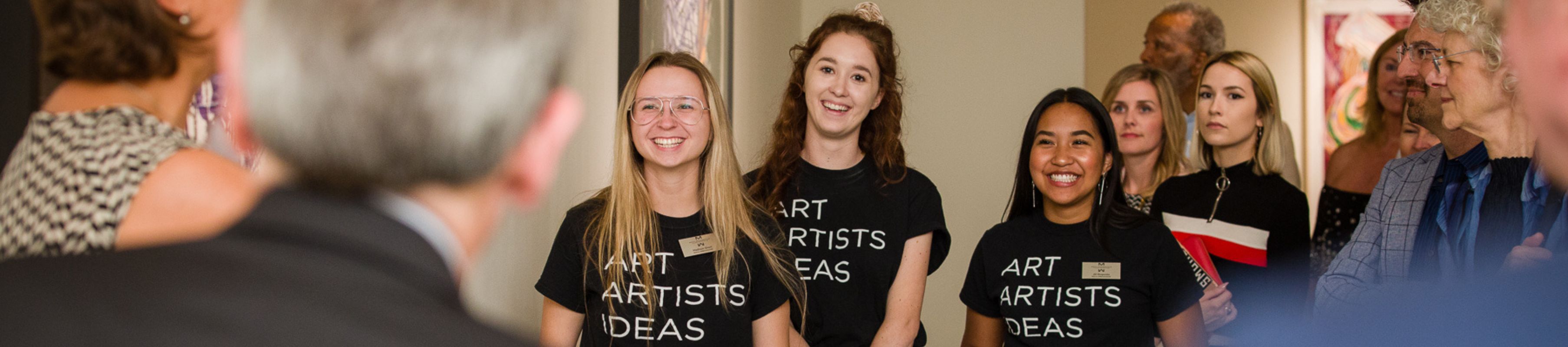 three MOCA interns smiling and laughing at an artist talk during an exhibition opening