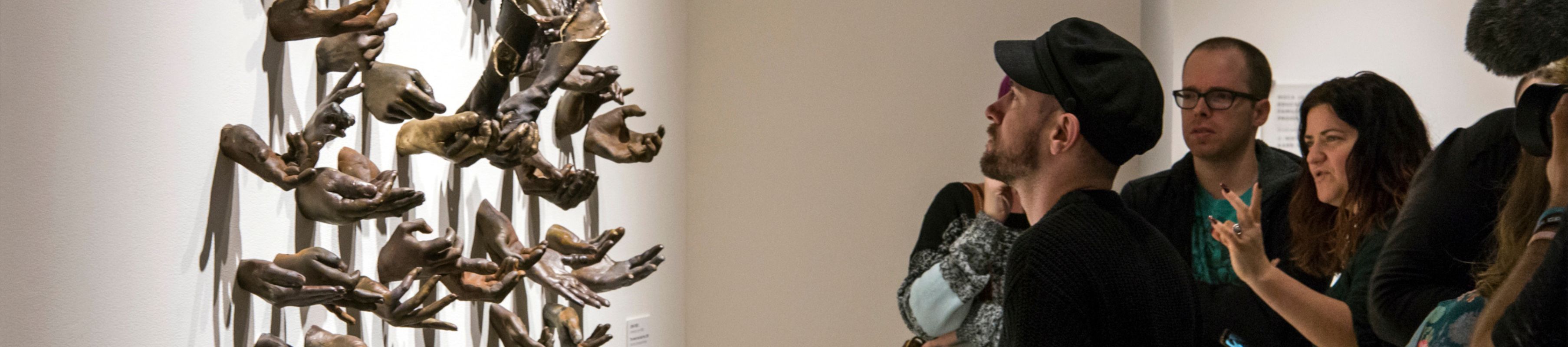 college student examines artwork of cast hands by UNF Student Artist-in-Residence Jenn Peak