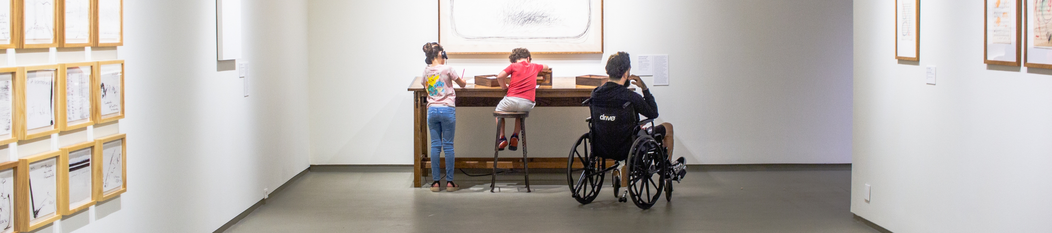 two children and a man in a wheelchair engaging in an interactive art piece at a table